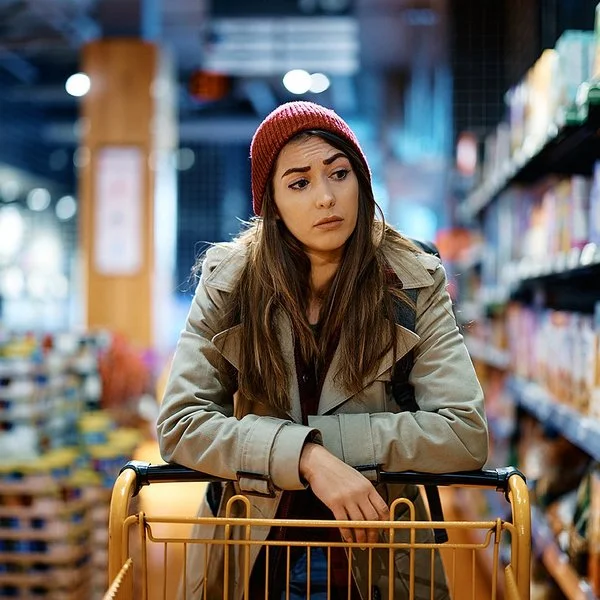 Eine Frau schiebt einen Einkaufswagen und schaut kritisch auf die Supermarktregale.