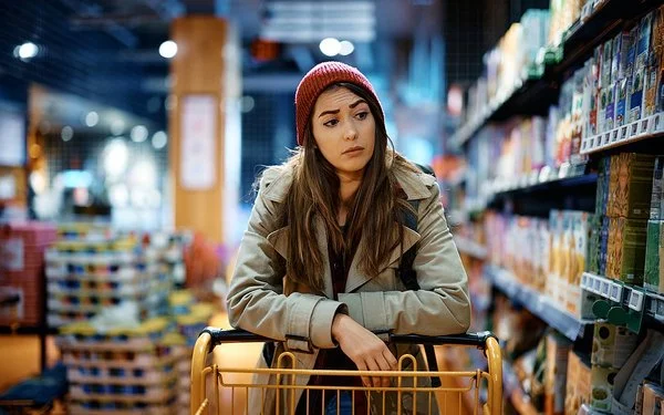 Eine Frau schiebt einen Einkaufswagen und schaut kritisch auf die Supermarktregale.