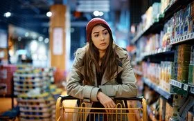 Eine Frau schiebt einen Einkaufswagen und schaut kritisch auf die Supermarktregale.