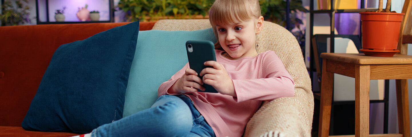 Ein Mädchen spielt mit einem Smartphone und ist dabei Werbung ausgesetzt.