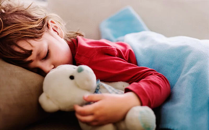 Ein Mädchen mit Pfeifferschem Drüsenfieber liegt mit einem Teddybären im Bett und schläft.