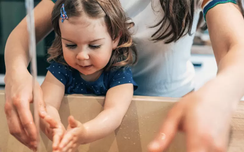 Ein kleines Mädchen wäscht sich mit der Hilfe einer erwachsenen Person an einem großen Waschbecken die Hände.