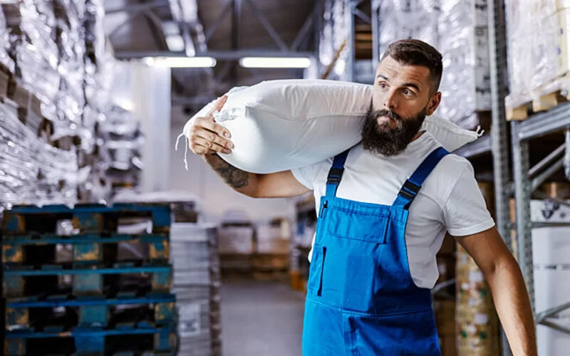 Junger Mann macht eine Ausbildung und schleppt einen Sack Mehl auf seinen Schultern.