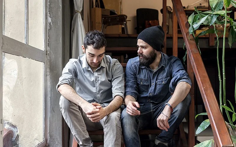 Zwei junge Männer sitzen auf einer Treppe und unterhalten sich über ihre mentale Gesundheit.