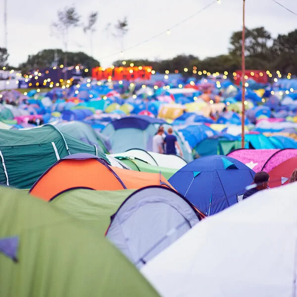 Aufnahme eines Campingplatzes mit vielen bunten Zeltdächern auf einem Outdoor-Festival. Über den Zelten hängen Lichterketten.