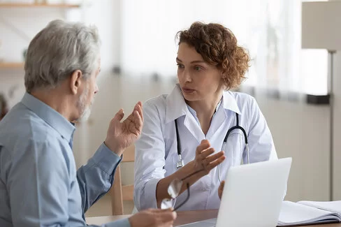 Eine Ärztin spricht mit einem älteren männlichen Patienten. Der Patient sitzt entspannt und hört aufmerksam zu, während die Ärztin ihm etwas erklärt.