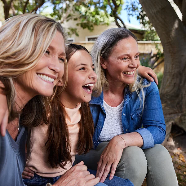 Ein Mädchen sitzt zwischen zwei älteren Frauen, alle lachen gemeinsam.