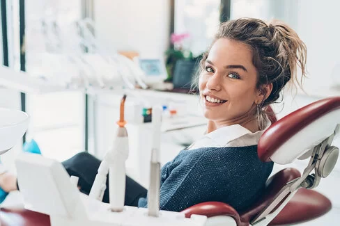 Eine junge Frau liegt auf einem Zahnarztstuhl und lächelt zufrieden. Ihre Patientendaten sind bei der AOK-Zahnklinik in guten Händen.