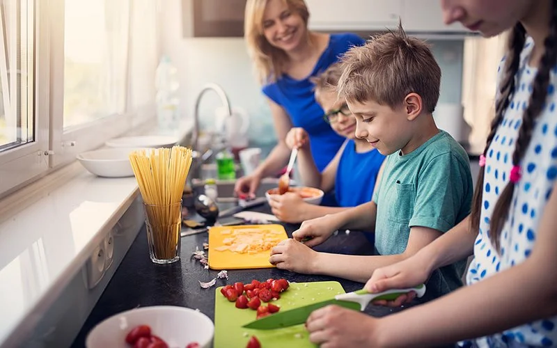 Eine Mutter und drei Kinder schnippeln in der Küche Tomaten und Käse.