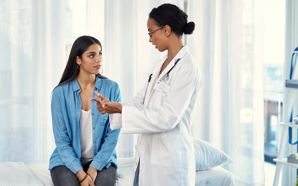 Eine Frau im weißen Arztkittel erklärt einer anderen Frau etwas.