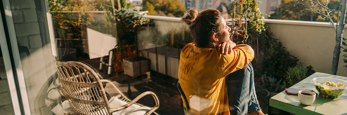 Ein junge Frau genießt die Morgensonne auf ihrem Balkon