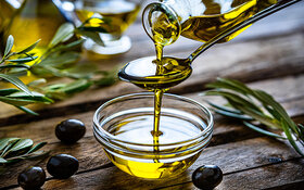 Jemand misst Olivenöl mit einem Löffel in eine kleine Schale ab.