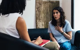 Eine junge Frau spricht mit ihrer Therapeutin, die nur von hinten zu sehen ist, während einer psychotherapeutischen Einzelsitzung.