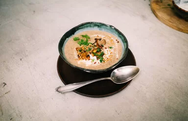 Champignoncremesuppe mit knusprigem Buchweizentopping nach einem Rezept von Felicitas Then, angerichtet auf einem schwarzen Teller, garniert mit Petersilie und Sauerrahm.