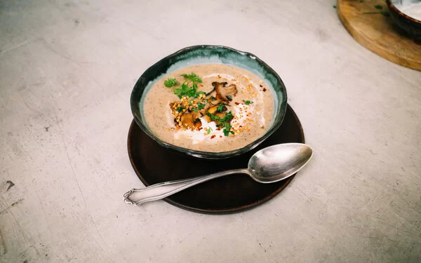 Champignoncremesuppe mit knusprigem Buchweizentopping nach einem Rezept von Felicitas Then, angerichtet auf einem schwarzen Teller, garniert mit Petersilie und Sauerrahm.