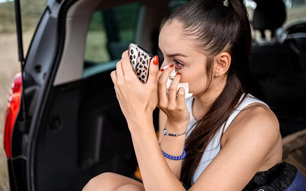 Eine Frau benutzt ihre Handykamera, um ihr Auge zu betrachten, das sie mit einem Taschentuch betupft.