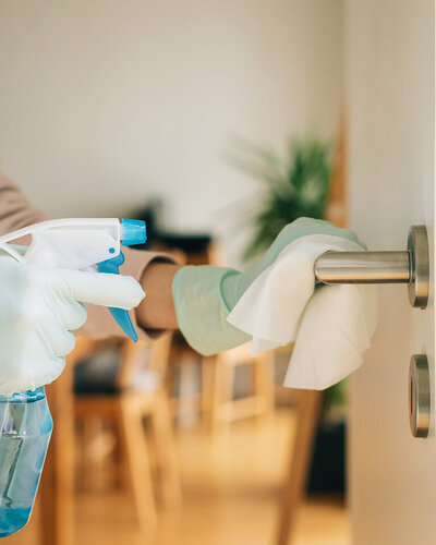 Pflegende Person achtet auf korrekte Hygiene in der Pflege und reinigt einen Türgriff.