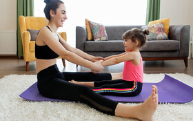Mutter macht gemeinsam mit ihrem Kind Sport auf dem Boden im Wohnzimmer.
