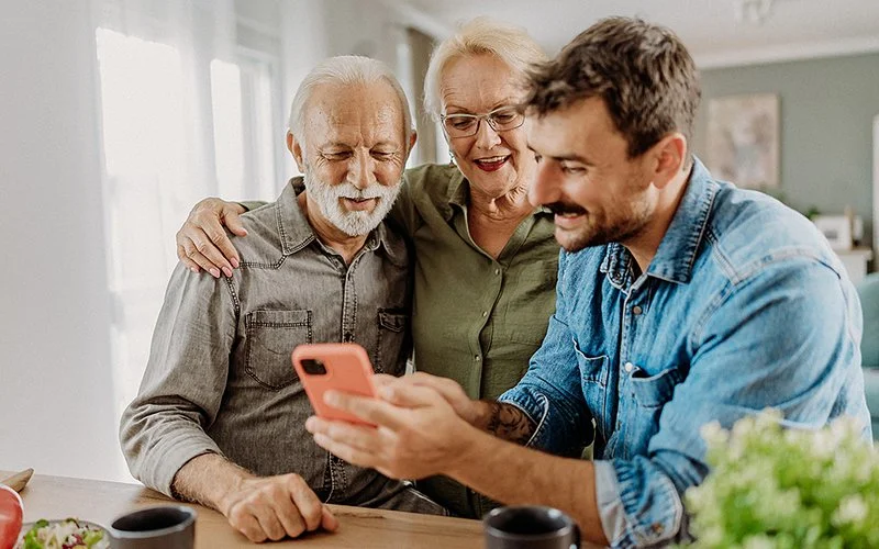 Ein jüngerer Mann zeigt einem älteren Paar etwas auf dem Smartphone.