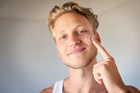 Ein junger Mann cremt sein Gesicht ein.