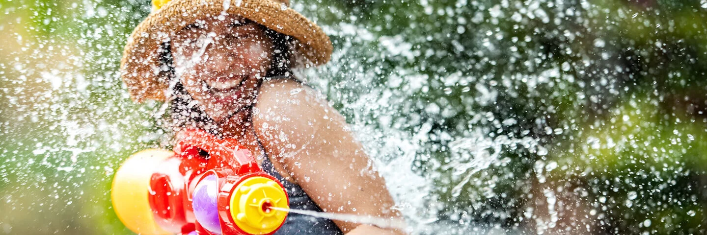 Eine junge Frau die einen Sonnenhut trägt, schießt mit einer Wasserpistole auf eine andere Person.