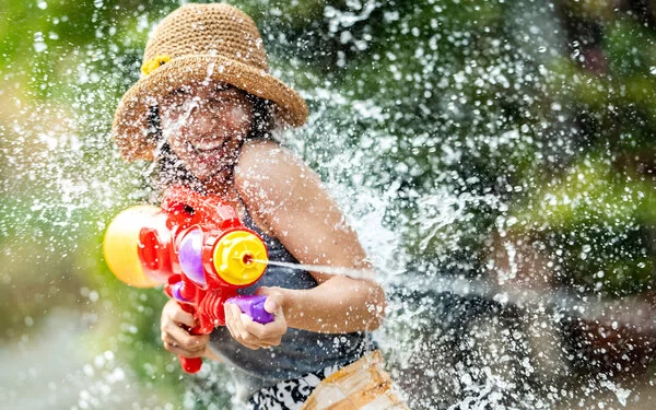 Eine junge Frau die einen Sonnenhut trägt, schießt mit einer Wasserpistole auf eine andere Person.