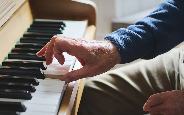 Nahaufnahme der Hand eines alten Mannes, die Klavier spielt.