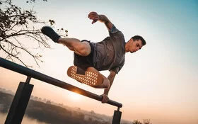 Mann übt draußen Parkour-Sport aus und springt über ein Geländer.