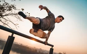 Mann übt draußen Parkour-Sport aus und springt über ein Geländer.