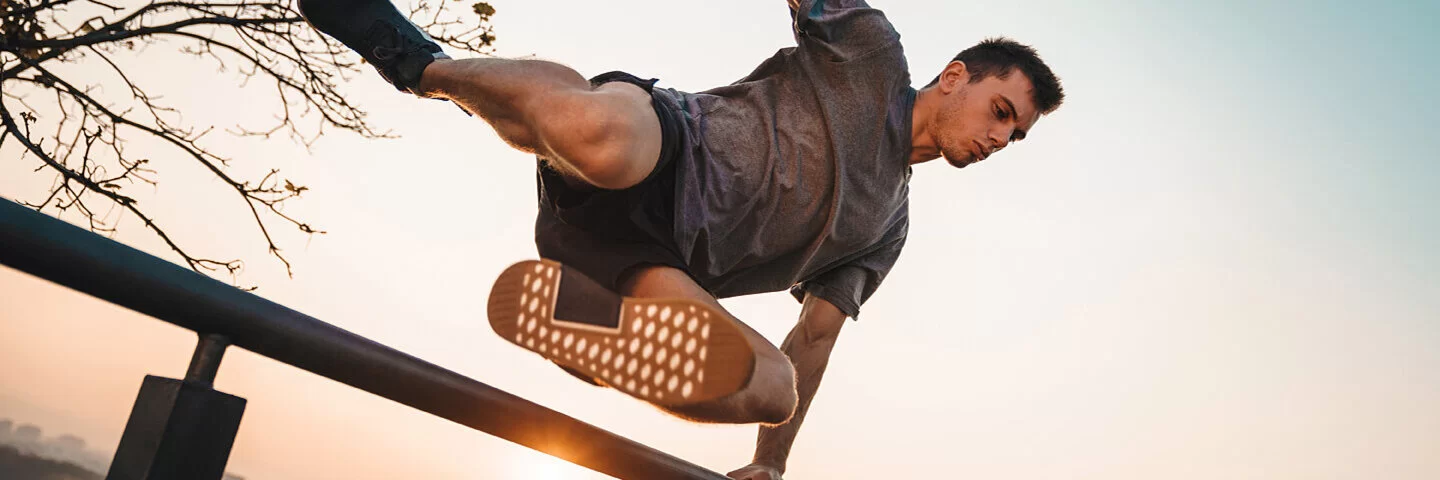 Mann übt draußen Parkour-Sport aus und springt über ein Geländer.