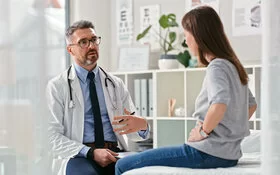 Eine Frau mit einem Zwölffingerdarmgeschwür sitzt auf einer Behandlungsliege während sie mit ihrem Arzt spricht.