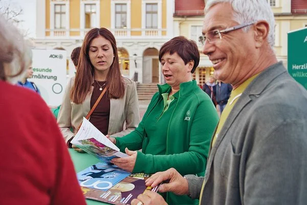 Mehrere Personen stehen an einem Messetisch und unterhalten sich mit einer AOK-Mitarbeiterin.
