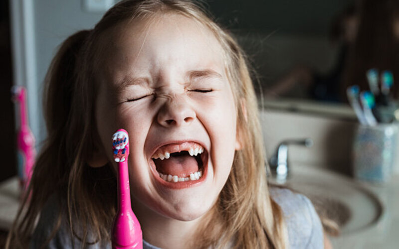 Kleines Mädchen mit Zahnlücke putzt sich die Zähne – welche Zahnbürste ist dafür am besten geeignet?