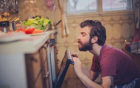 Ein Mann, der sich gesund ernährt, hat den Backofen geöffnet und blickt hinein.