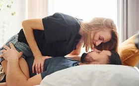 Eine Frau sitzt im Bett auf ihrem Mann.