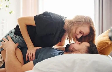 Eine Frau sitzt im Bett auf ihrem Mann.