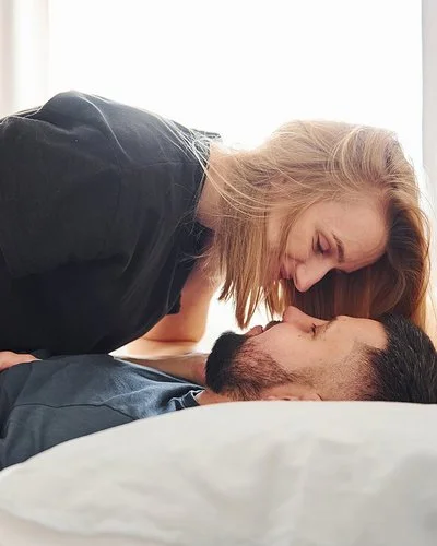 Eine Frau sitzt im Bett auf ihrem Mann.