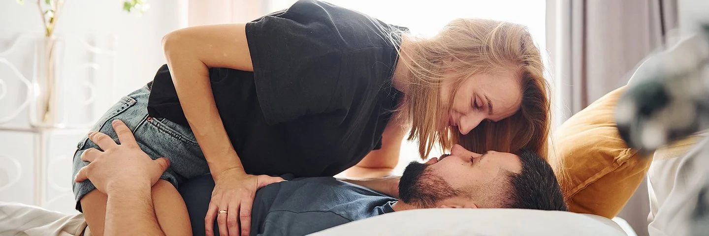 Eine Frau sitzt im Bett auf ihrem Mann.