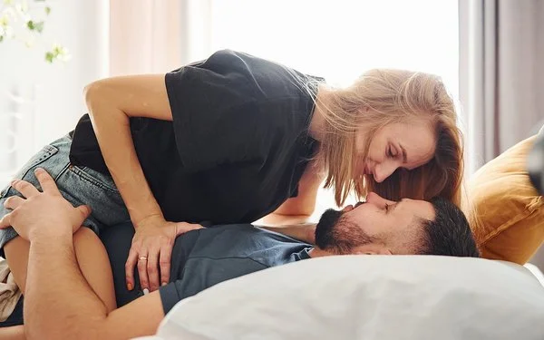 Eine Frau sitzt im Bett auf ihrem Mann.