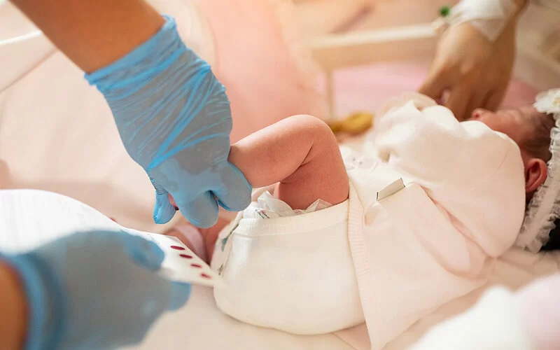 Eine Kinderkrankenschwester lässt beim erweiterten Neugeborenen-Screening wenige Blutstropfen aus der Ferse eines Neugeborenen auf eine spezielle Papierkarte tropfen.