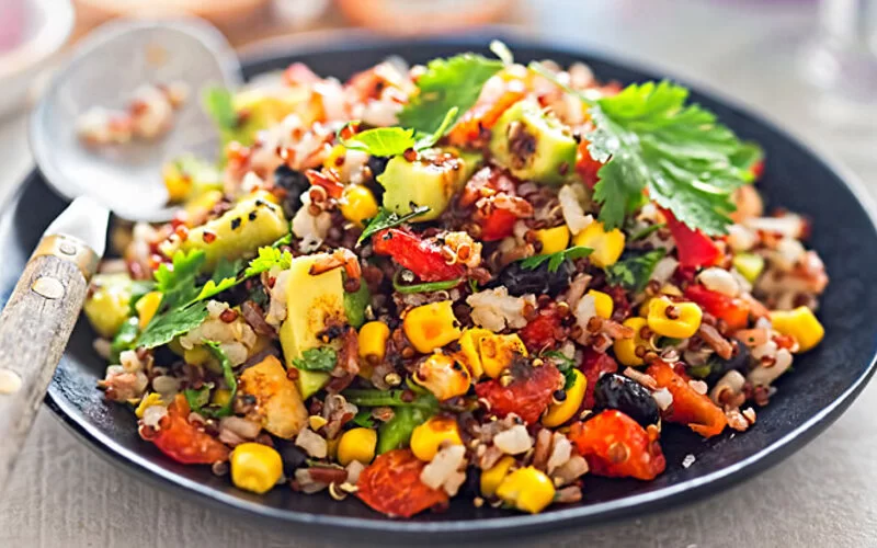 Ein Salat, der aus Bohnen, Avocado, Mais, Tomate, Reis und Quinoa mit Chili-Dressing besteht.