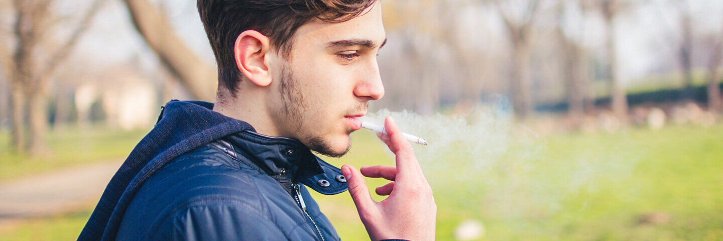 Ein junger Mann raucht eine Zigarette im Park.