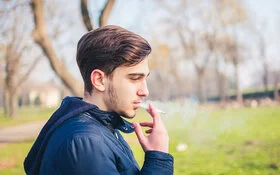 Ein junger Mann raucht eine Zigarette im Park.