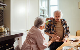 Ein älterer Mann steht mit seiner Frau in Küche und hat durch eine Divertikulitis plötzliche Schmerzen im Unterbauch.
