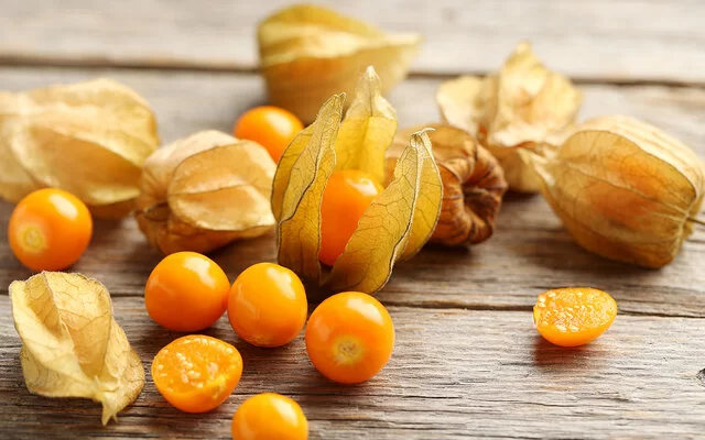 Mehrere Physalisfrüchte liegen auf einem hölzernen Untergrund.
