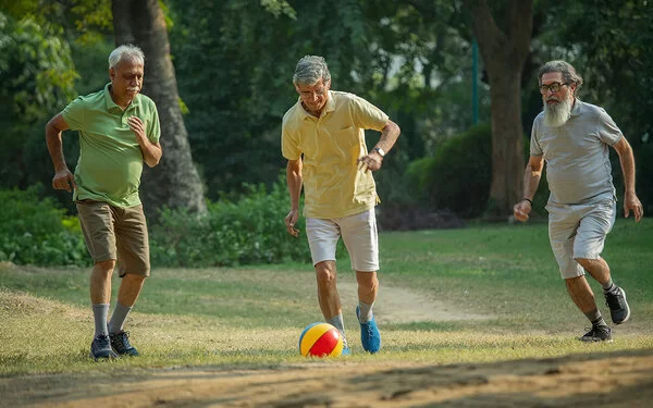 Drei ältere Männer spielen auf einer Wiese Walking Football, der mittlere Mann schießt gerade den Ball.
