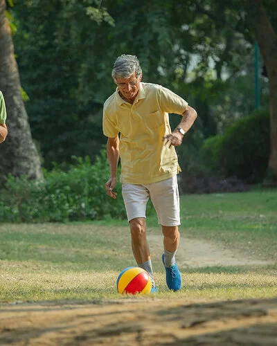 Drei ältere Männer spielen auf einer Wiese Walking Football, der mittlere Mann schießt gerade den Ball.