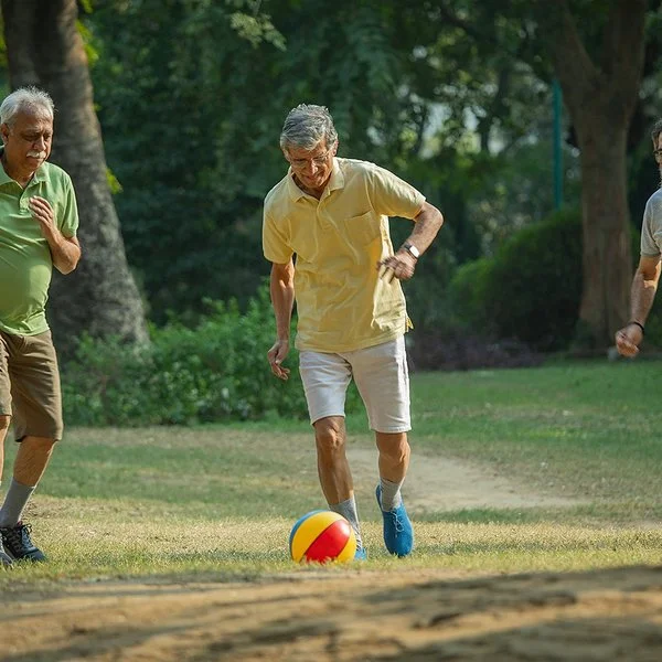 Drei ältere Männer spielen auf einer Wiese Walking Football, der mittlere Mann schießt gerade den Ball.