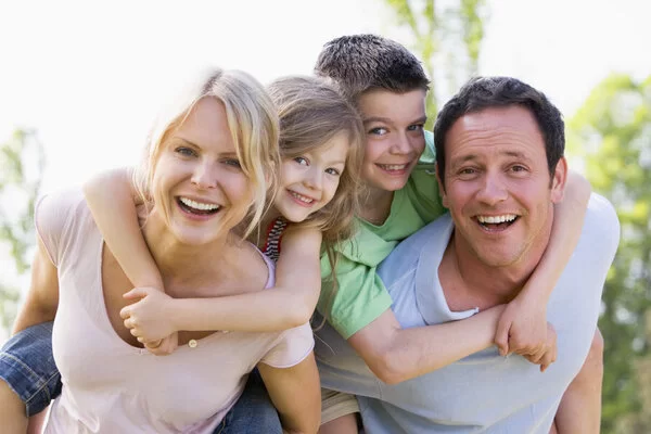 Familie ist unterwegs im Grünen. Vater und Mutter tragen je ein Kind Huckepack.