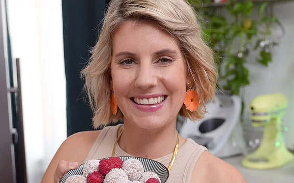 Felicitas Then hält einen kleinen Teller mit selbstgemachten Energy Balls und frischen Himbeeren in den Händen und lacht.